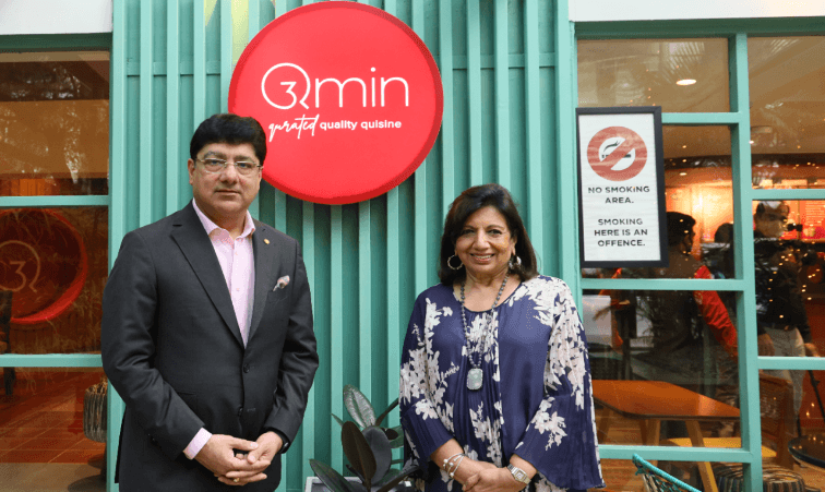 Two people standing outside Qmin restaurant with branding signage in the background.