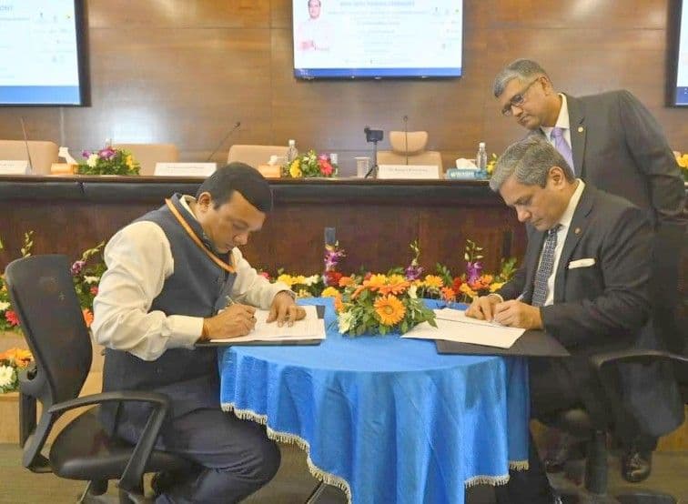 Two officials signing documents at a formal agreement ceremony with a third person overseeing.